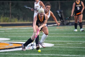 Field hockey players in action, competing on a grassy field in a competitive match.