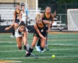 Girls playing field hockey, two players competing for the ball on a green field, intense match action captured.