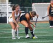 Two field hockey players in action competing for the ball on a turf field.