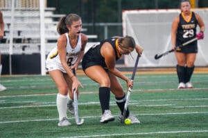 Two field hockey players in action competing for the ball on a turf field.