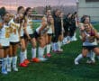High school girls' field hockey team in uniform on the field, smiling and posing before a game at sunset.