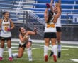 Field hockey team celebrates a victory with smiles and cheers on a rainy sports field.