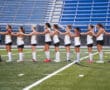 Field hockey team in white jerseys lined up on the field, preparing for a match with unity and focus.