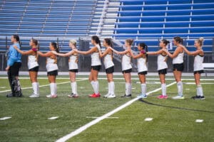 Field hockey team in white jerseys lined up on the field, preparing for a match with unity and focus.