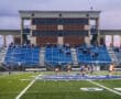 Field hockey game at Spartan Stadium during overcast weather with players in motion and spectators in the stands.
