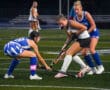 Field hockey players in action on a turf field during a competitive match.