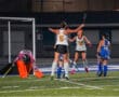 Field hockey players celebrating a goal in a nighttime match.