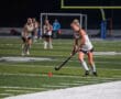 Field hockey player dribbling under the stadium lights during a night match with red ball in focus.
