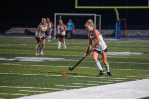 Field hockey player dribbling under the stadium lights during a night match with red ball in focus.