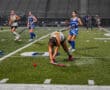 Field hockey players compete intensely in rain on a synthetic field, focusing on a red ball.