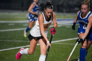 Girls playing intense field hockey match on turf, focusing on player in black and white jersey with the ball.