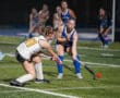 Field hockey players competing in an intense match under bright stadium lights.