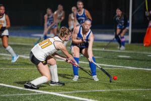 Field hockey players competing in an intense match under bright stadium lights.