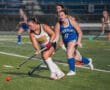 Field hockey players in action, Tigers vs. Spartans, competing for the ball on a turf field at night.