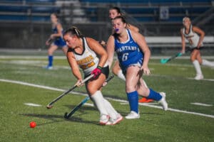Field hockey players in action, Tigers vs. Spartans, competing for the ball on a turf field at night.