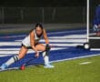 Field hockey player drives ball near goal in intense night match.