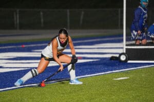 Field hockey player drives ball near goal in intense night match.