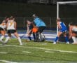 Field hockey players compete near goal, intense night match.
