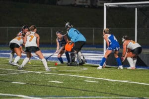 Field hockey players compete near goal, intense night match.