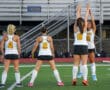 Four female field hockey players in warm-up on a field, numbered jerseys visible.