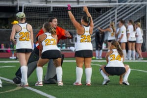 Field hockey team strategizing on the field during a break in the game.