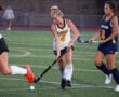 Field hockey players competing intensely during a match on a green turf field.