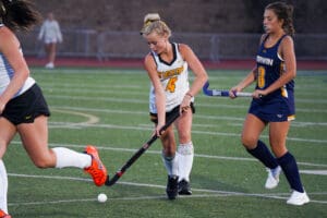 Field hockey players competing intensely during a match on a green turf field.