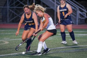 Two female field hockey players compete for the ball on a green turf field during a game.