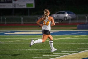 Female field hockey player in action, wearing jersey number 34 on a sports field at night.