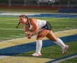 Field hockey player in action, swinging stick on a brightly lit turf field at night.