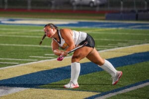 Field hockey player in action, swinging stick on a brightly lit turf field at night.