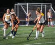 Field hockey players competing under lights on a turf field, with focus on two players in action.