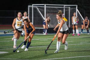 Field hockey players competing under lights on a turf field, with focus on two players in action.