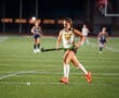 Field hockey player in action, dribbling ball at night game on turf field.