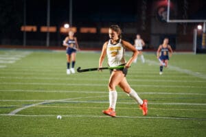 Field hockey player in action, dribbling ball at night game on turf field.