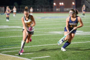 Field hockey players in action during a nighttime match, showcasing skills on a well-lit turf field.