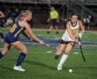 Field hockey players competing during a match on a green turf field.