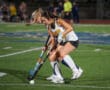 Field hockey players competing for the ball during a match on a green turf field.