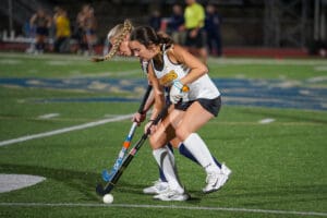 Field hockey players competing for the ball during a match on a green turf field.