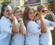 Four smiling girls in matching t-shirts posing with flexed arms outdoors.