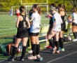 Field hockey players take a break on the sidelines during a game on a sunny day.