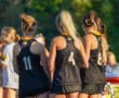 Girls in black sports jerseys wait on the field, ready for a team activity in the sunshine.