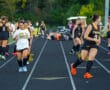 Girls warming up for field hockey practice on a track, wearing sports uniforms and gear.