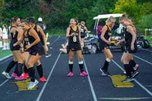 Field hockey team warming up with footwork drills on a track.