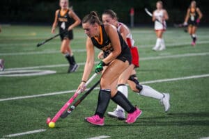 Field hockey players in action during a match on a green turf field.