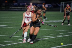 Two field hockey players competing intensely for the ball on a green field.
