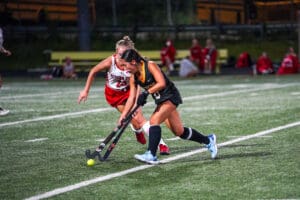 Two field hockey players compete for the ball on a green turf field during an intense match.