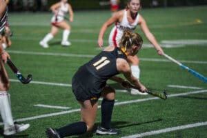 Field hockey player in black jersey tackling during a night match on a green field.