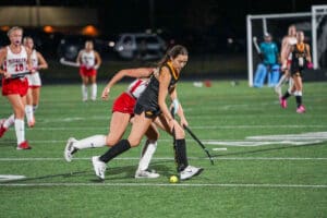 Girls engaged in a competitive field hockey match at night, focused on controlling the ball on the field.