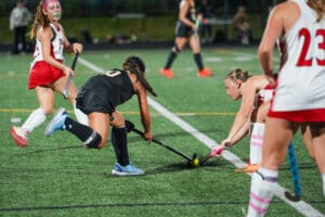 Field hockey players compete intensely for the ball on a bright green turf under stadium lights.